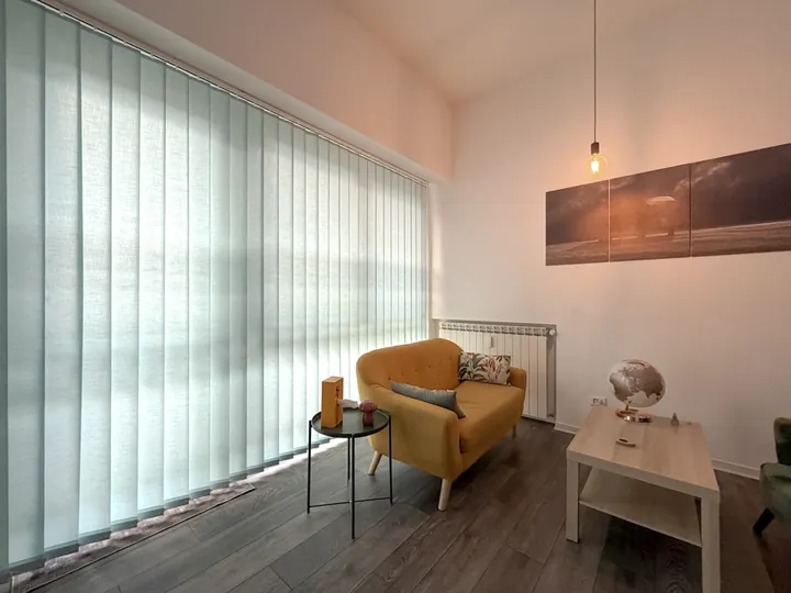 Divano giallo accanto alla vetrata con tende chiare nello studio di psicoterapia a Roma Eur